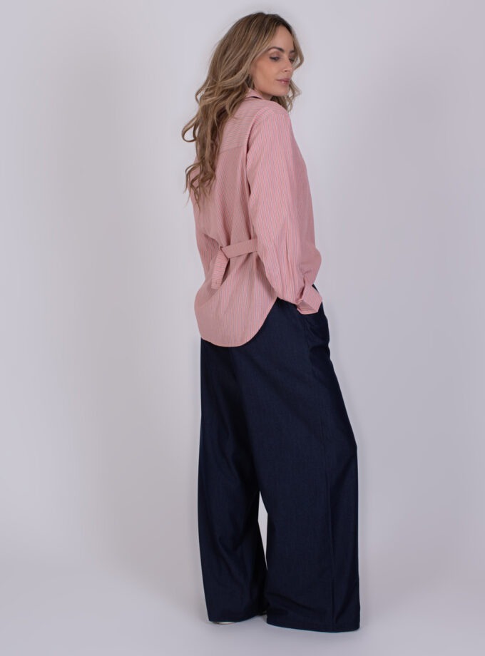 Vrouw in een roze gestreeerde blouse genaamd "Chennai old pink" en donkerblauwe wijde broek poseert zijwaarts tegen een neutrale achtergrond.