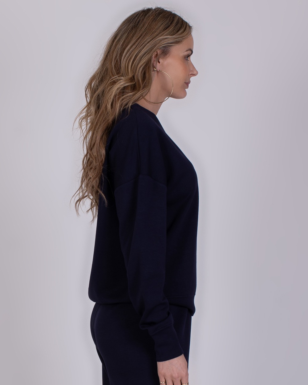 Chester navy 2 Vrouw in profiel die een donkerblauwe Chester Navy sweater en broek draagt tegen een neutrale achtergrond.