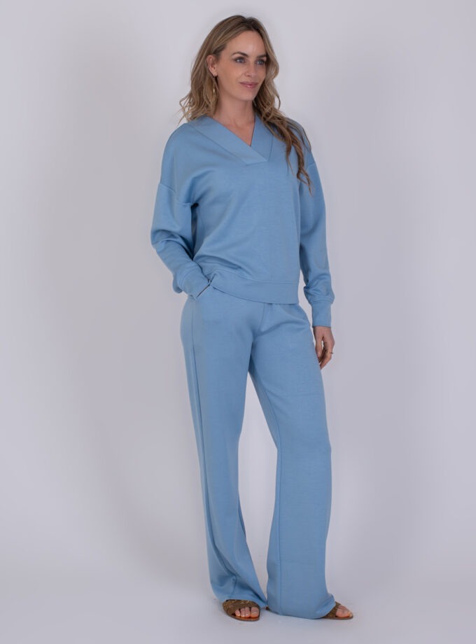 Vrouw draagt een comfortabele, lichtblauwe Chester soft blue loungewear-set met lange broek en V-hals trui.