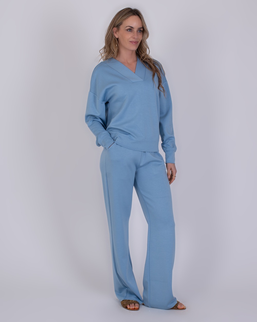 Chester soft blue 2 Vrouw draagt een comfortabele, lichtblauwe Chester soft blue loungewear-set met lange broek en V-hals trui.