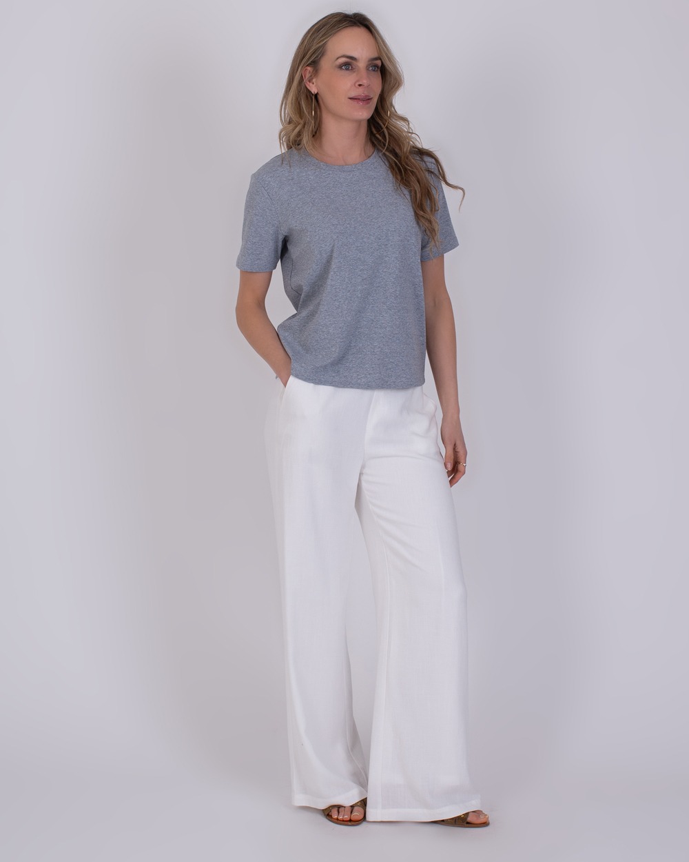 Denver grey 2 Vrouw draagt een grijs Denver Grey T-shirt met korte mouwen en witte, wijde broek.