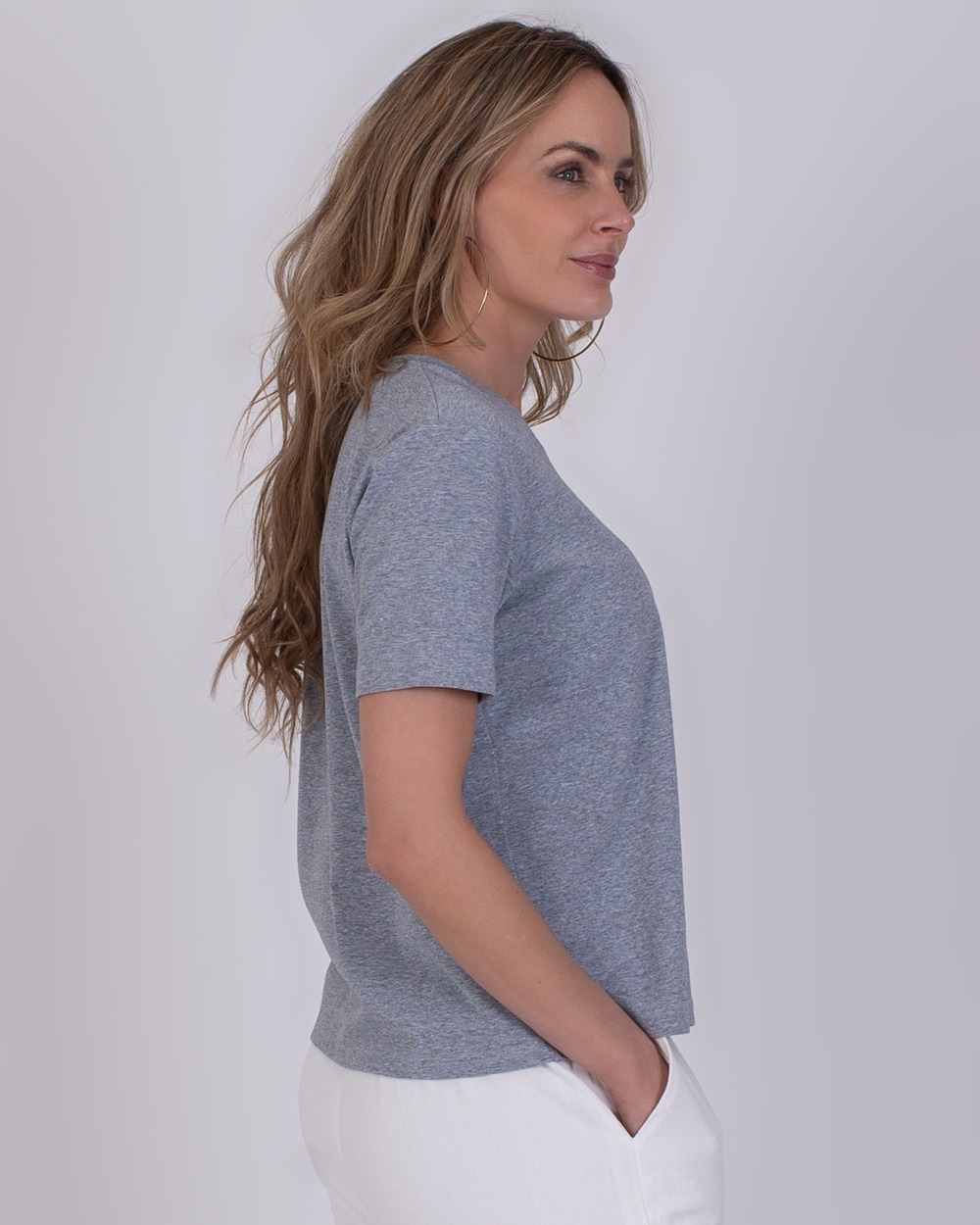 Denver grey 3 Vrouw in zijaanzicht draagt een Denver grey T-shirt en witte broek tegen een neutrale achtergrond.