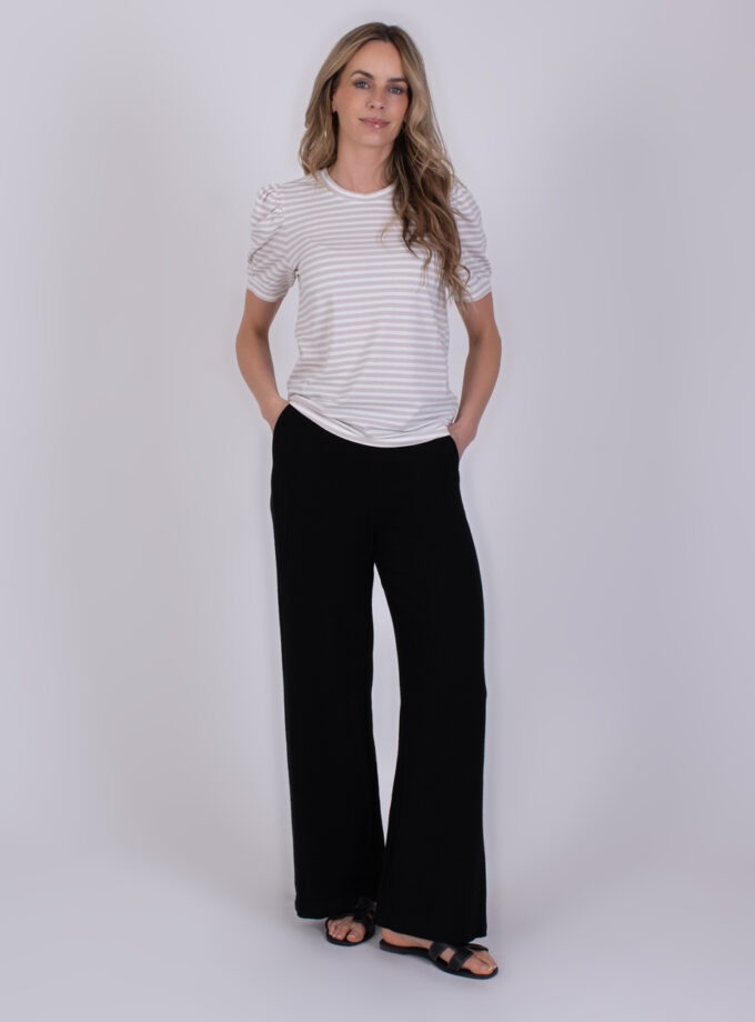 Vrouw draagt een Dhaka stripe grey – offwhite gestreept T-shirt met korte mouwen en zwarte broek.