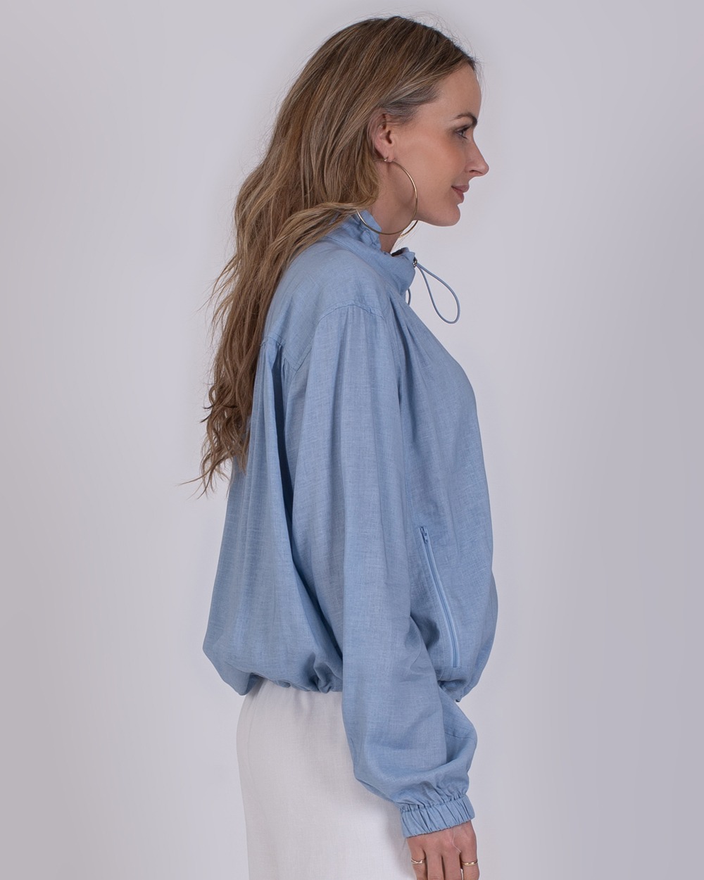 Edessa soft blue 2 Vrouw in profiel met een lichtblauwe Edessa-soft-blue-blouse met hoge kraag en strikdetail.
