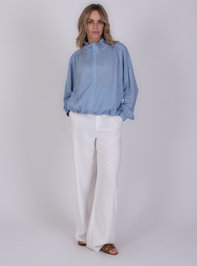 Vrouw draagt een lichtblauwe Edessa soft blue blouse met witte, wijde broek en sandalen.