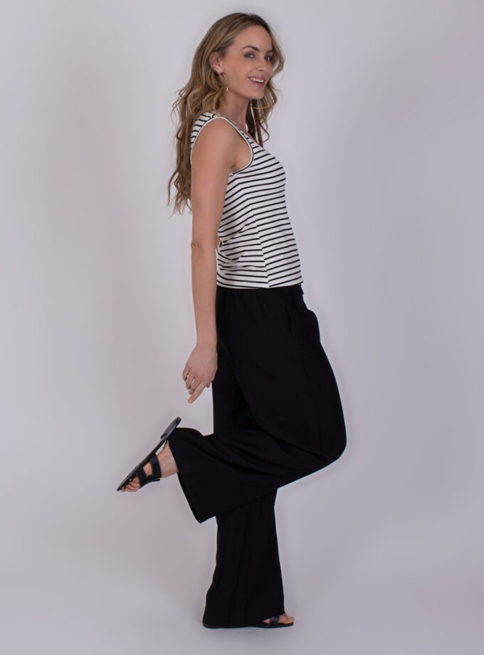 Vrouw poseert zijwaarts in een mouwloos Felize stripe black-offwhite top met zwarte broek en sandalen.