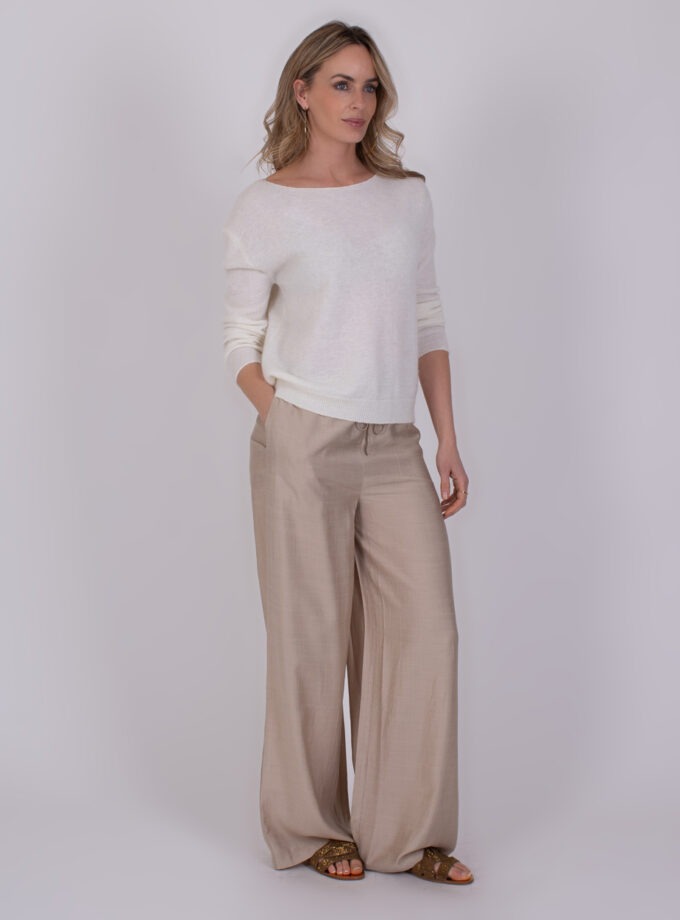 Vrouw draagt een off-white trui genaamd Granada en beige, wijde broek met sandalen.