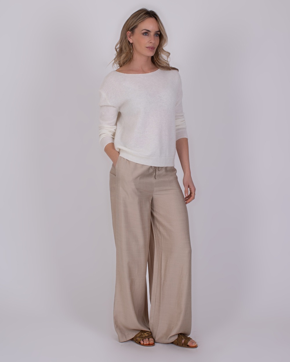 Vrouw draagt een off-white trui genaamd Granada en beige, wijde broek met sandalen.