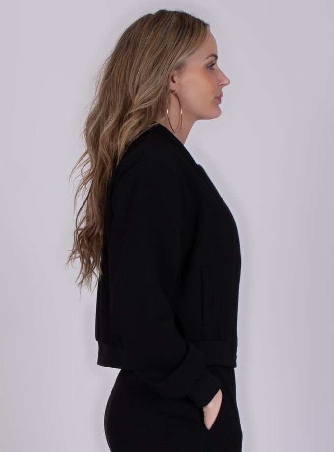 Vrouw in zijaanzicht draagt een zwarte Harlow Black 3 trui met haar hand in haar broekzak.