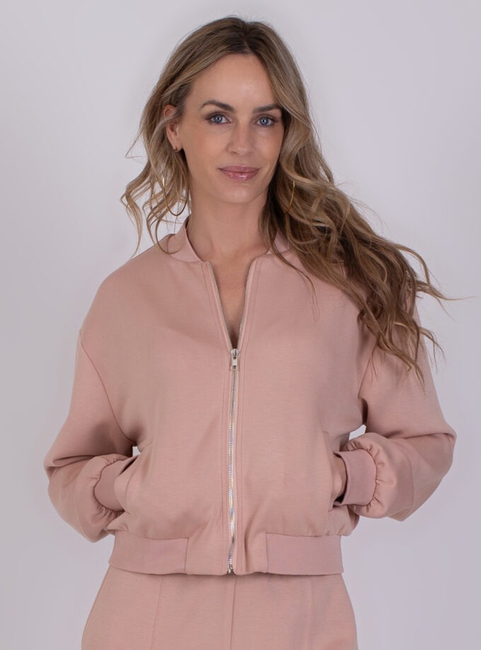 Vrouw draagt een Harlow bomberjack in oudroze met rits en steekzakken.