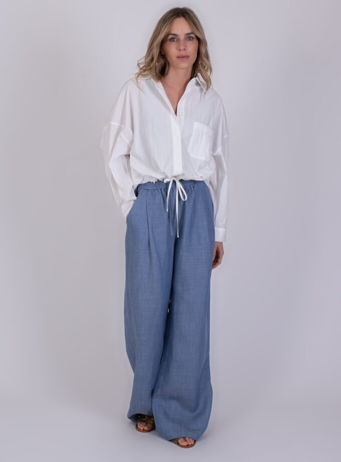 Vrouw draagt een offwhite blouse genaamd Juba met een trekkoord in de taille, gecombineerd met wijde lichtblauwe broek.
