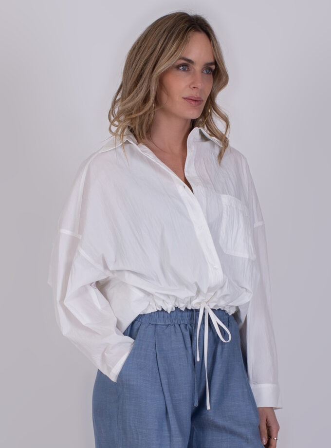 Vrouw draagt de Juba offwhite blouse met trekkoord en blauwe broek.