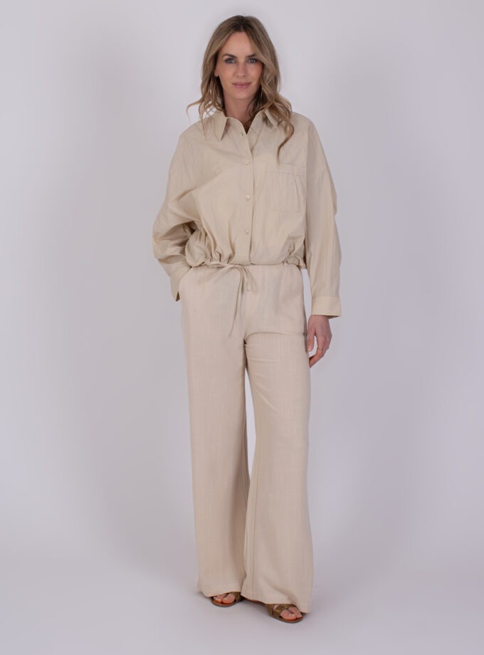 Vrouw draagt een beige Juba Pale 2 jumpsuit met lange mouwen en wijde pijpen.