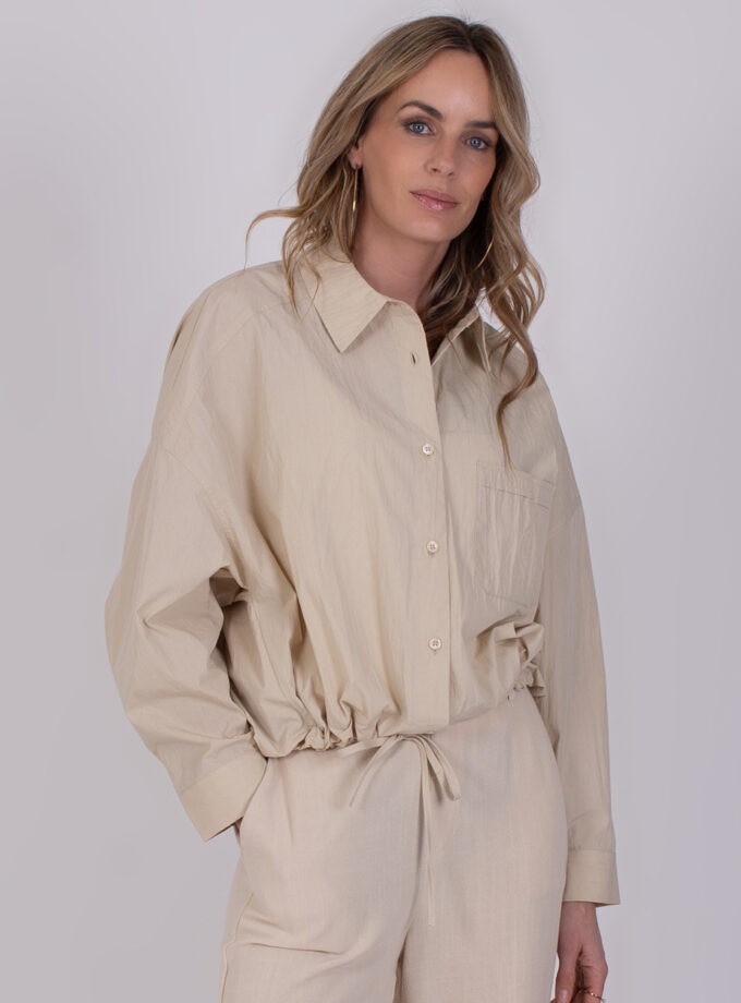 Vrouw draagt een beige Juba Pale 3 outfit met lange mouwen en trekkoord in de taille.