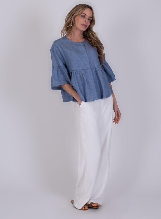 Vrouw draagt een Khost light jeans blue blouse met wijde mouwen en een witte, wijde broek.