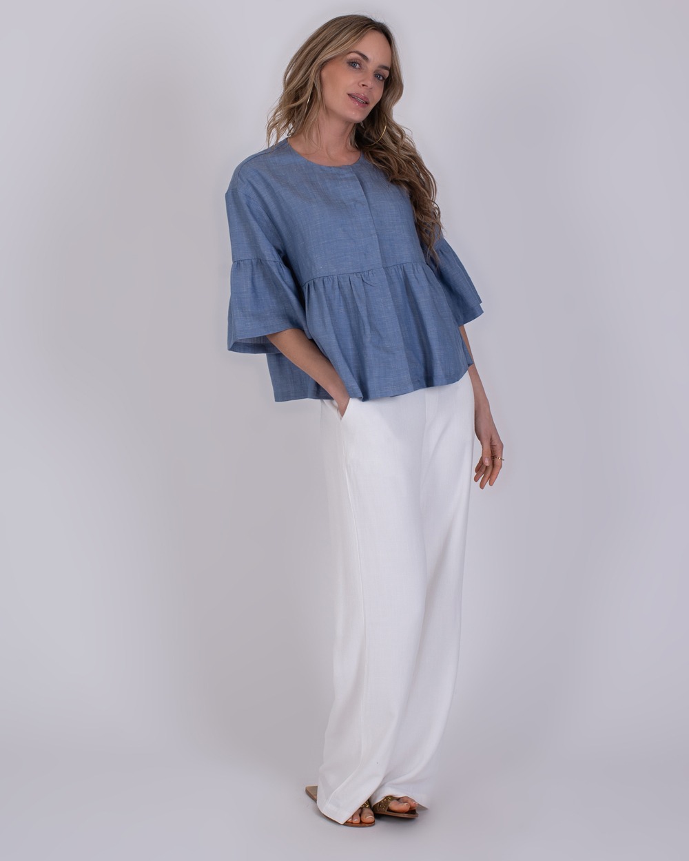 Vrouw draagt een Khost light jeans blue blouse met wijde mouwen en een witte, wijde broek.