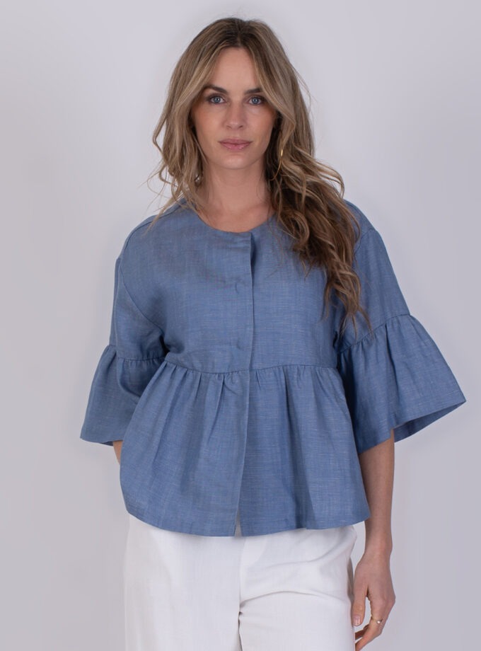 Vrouw draagt een blauwe Khost light jeans top met wijd uitlopende mouwen en witte broek.