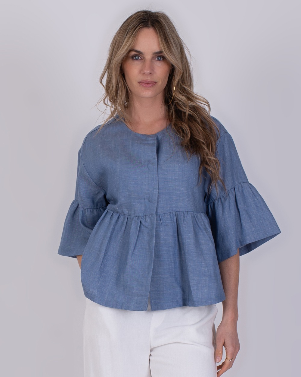 Khost light jeans blue 5 Vrouw draagt een blauwe Khost light jeans top met wijd uitlopende mouwen en witte broek.