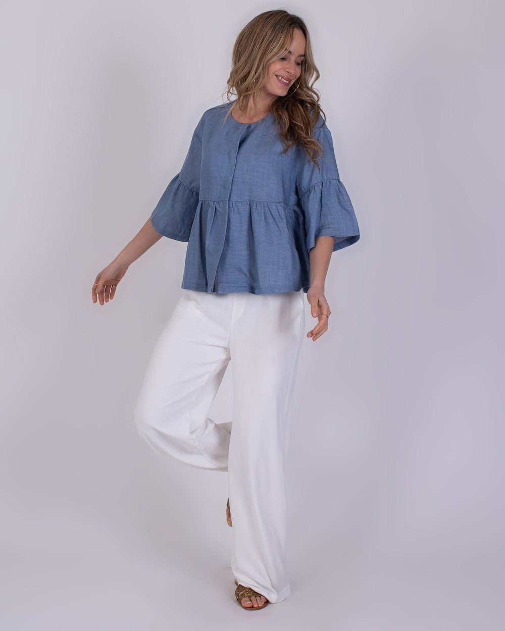 Khost light jeans blue Vrouw draagt een losse Khost light jeans blue top met wijde witte broek en sandalen.