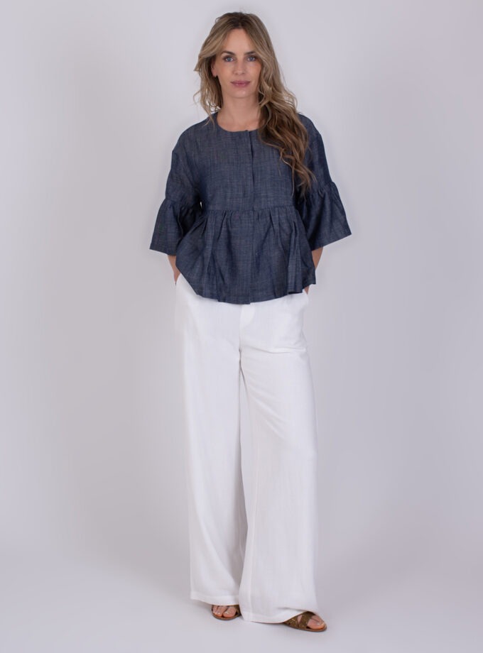 Vrouw draagt een Khost medium blue top met wijde driekwartsmouwen en witte, wijde broek.