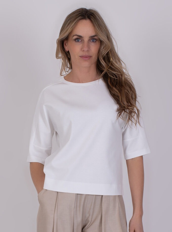 Vrouw draagt een Kiruna off white top met half lange mouwen en beige broek.