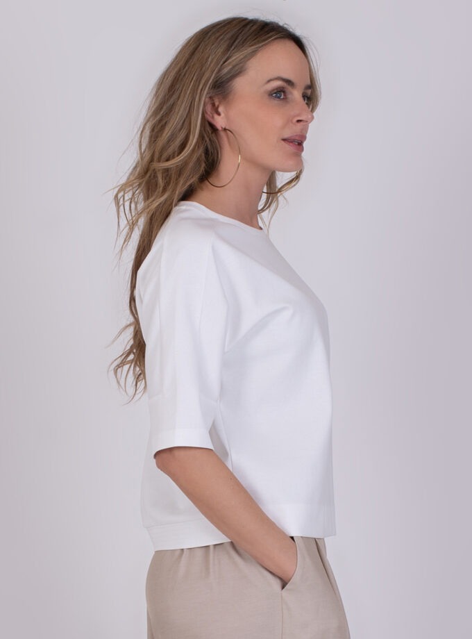 Vrouw in zijaanzicht draagt een Kiruna off white top met half lange mouwen en beige broek.