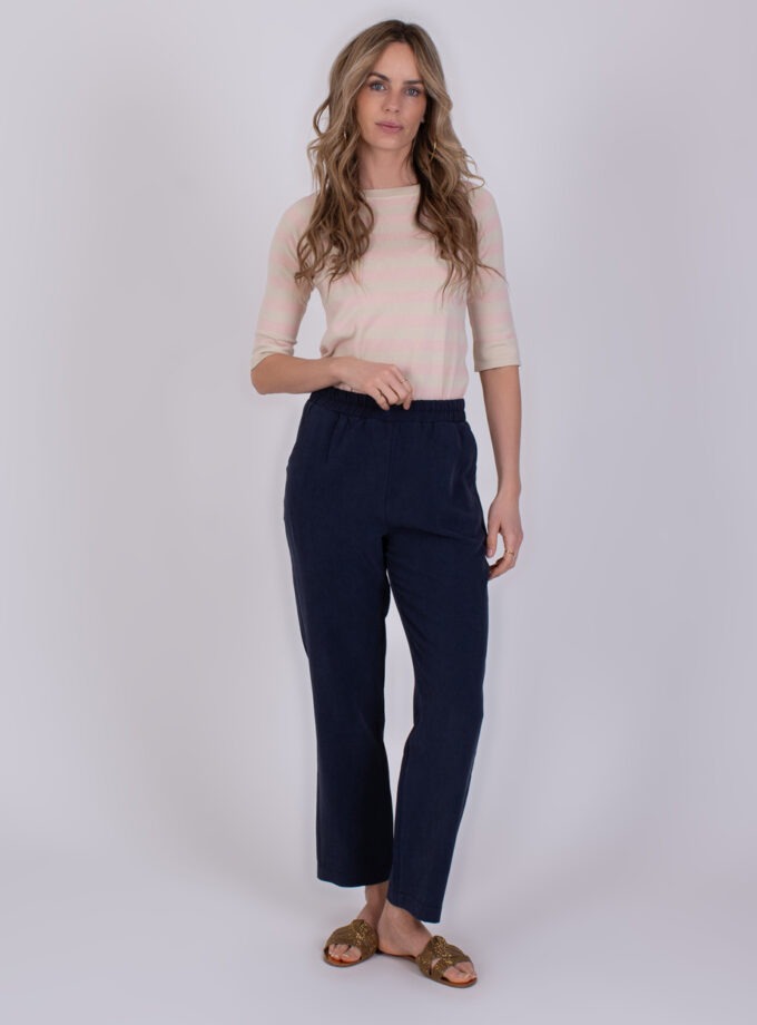 Vrouw draagt een lichtroze gestreepte top en een donkerblauwe Korcula navy broek met rechte pijpen.