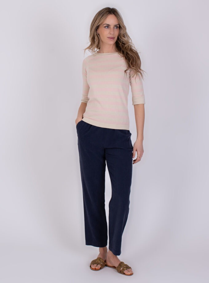 Vrouw draagt een licht gestreepte top en navy Korcula-broek met rechte pijpen.