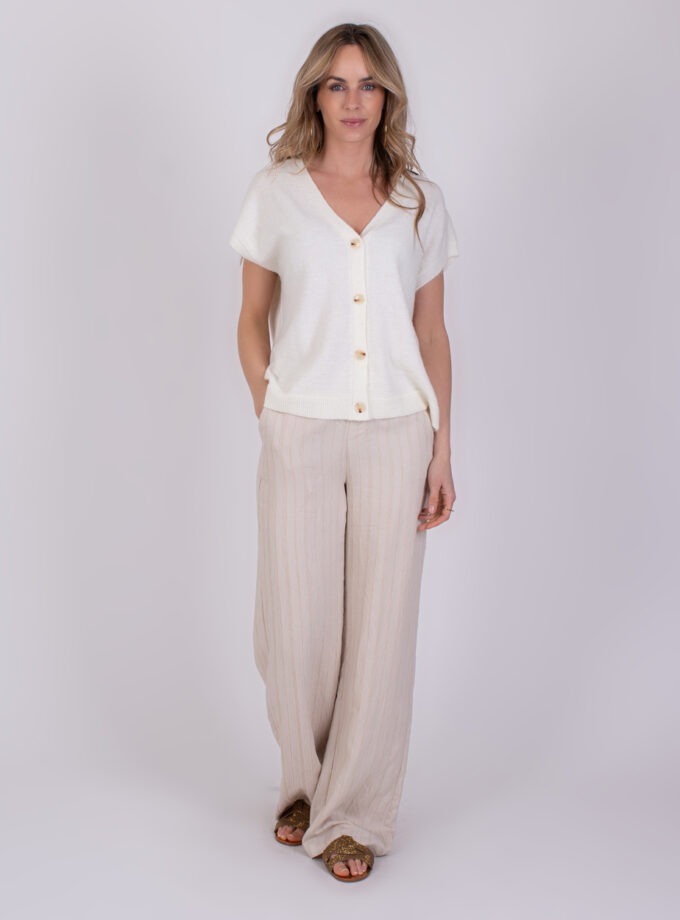 Vrouw draagt de off white 'Lamia' top met korte mouwen en knoopsluiting, gecombineerd met wijde beige broek.