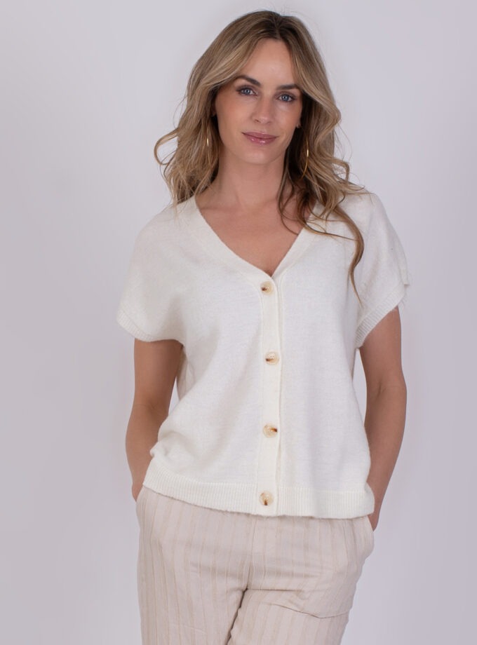 Vrouw draagt een offwhite Lamia-top met korte mouwen en knoopsluiting.