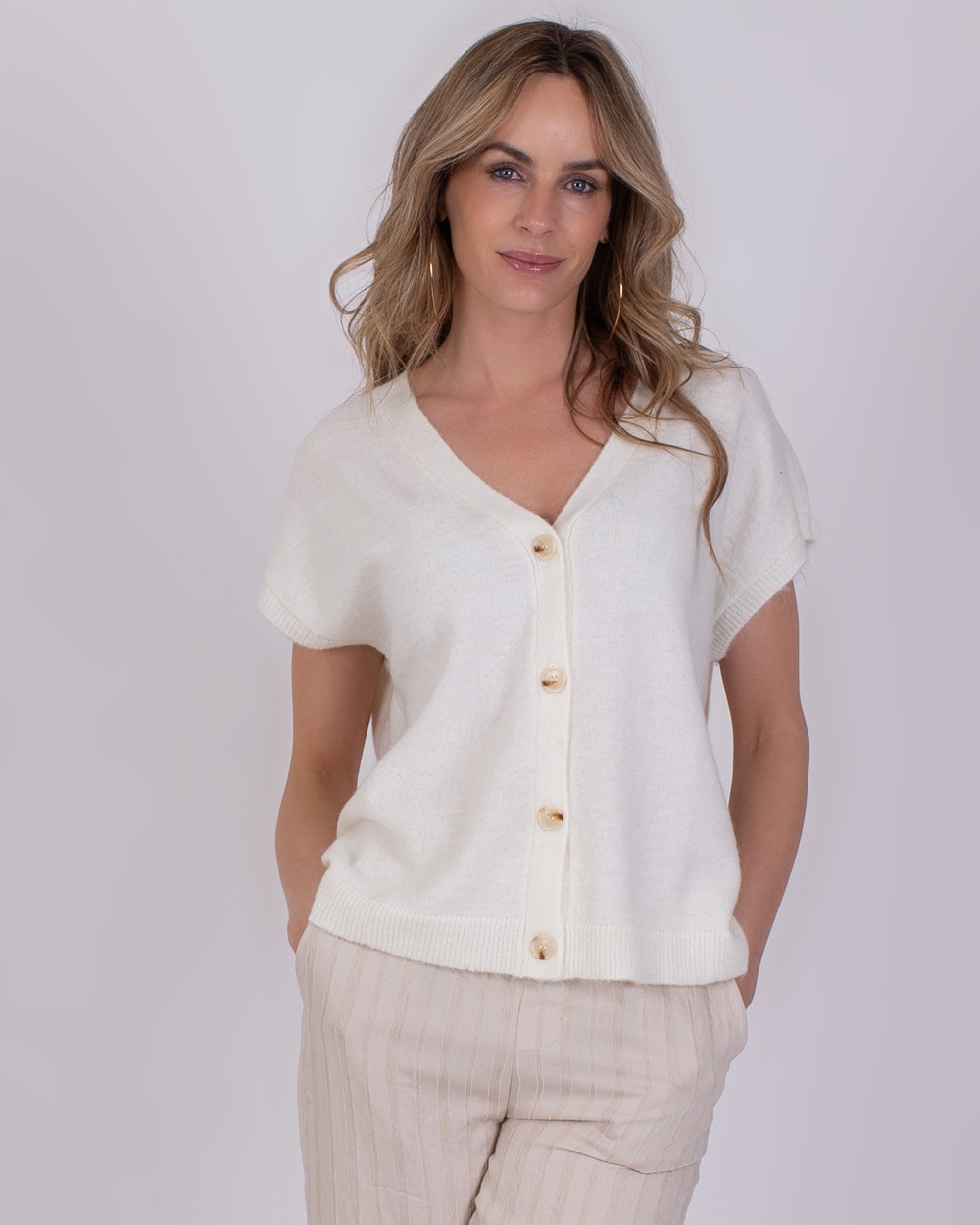 Vrouw draagt een offwhite Lamia-top met korte mouwen en knoopsluiting.