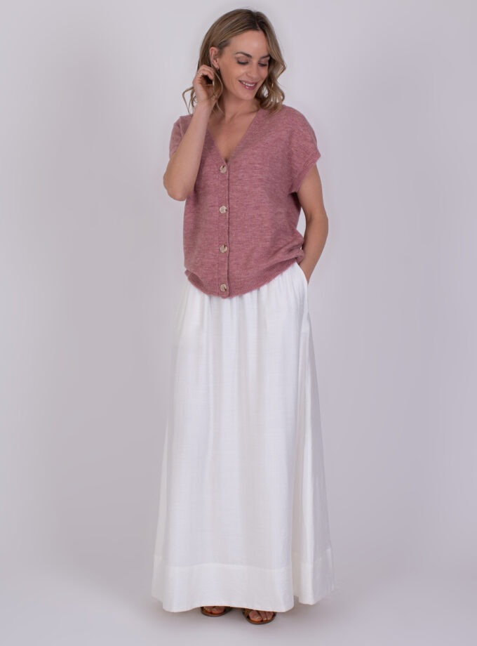 Vrouw draagt een roze Lamia Raspberry trui met knopen en een lange witte rok.