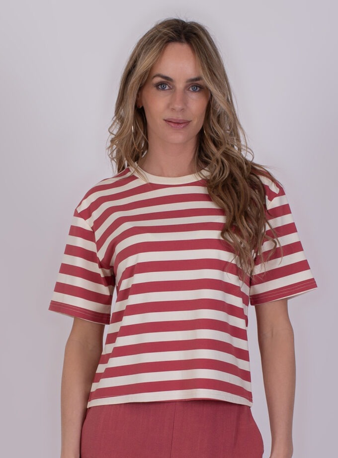 Vrouw met lang, golvend haar draagt een Larisa old pink gestreept T-shirt met korte mouwen en roze broek.