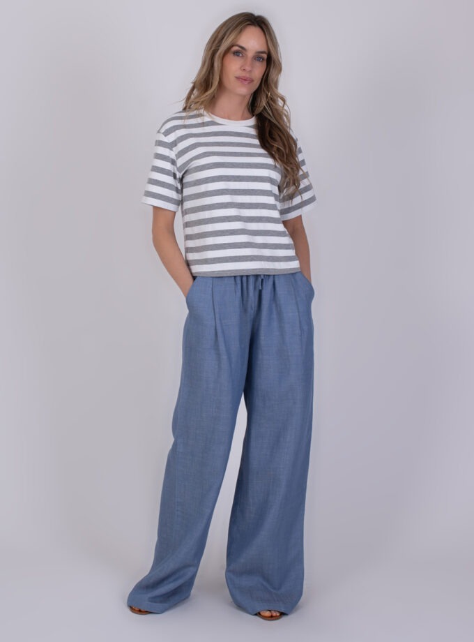 Vrouw draagt een grijs-wit gestreept Larisa T-shirt en een wijde lichtblauwe broek.