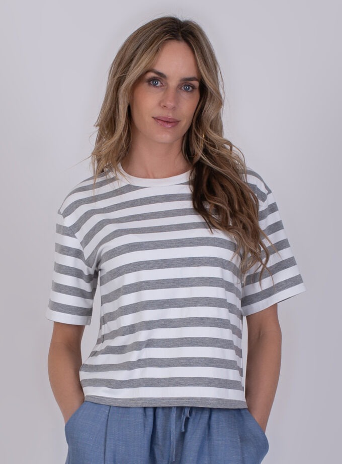 Vrouw draagt een Larisa stripe grey offwhite T-shirt met grijs-witte strepen en blauwe broek.
