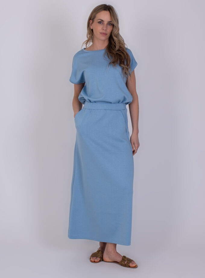 Vrouw draagt een lichtblauwe, losse Linz-jurk met korte mouwen en een lange rechte rok.