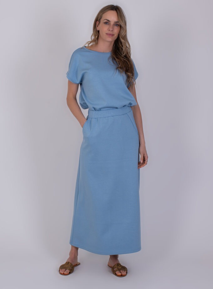 Vrouw draagt een lichtblauwe Linz soft blue outfit met korte mouwen en een lange rok.