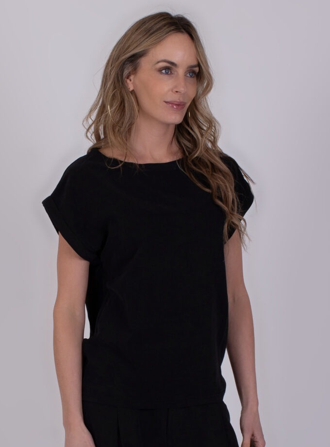 Vrouw draagt een zwarte Lodi top met opgerolde mouwen tegen een neutrale achtergrond.