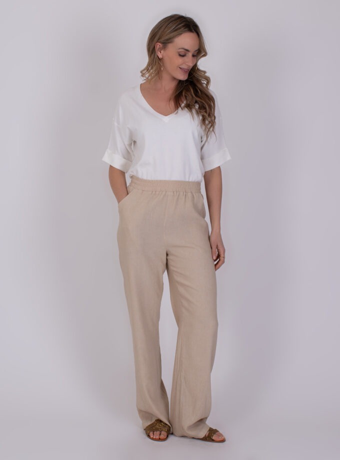 Vrouw draagt een witte top en beige linnen broek uit de Lome pale 2 collectie.