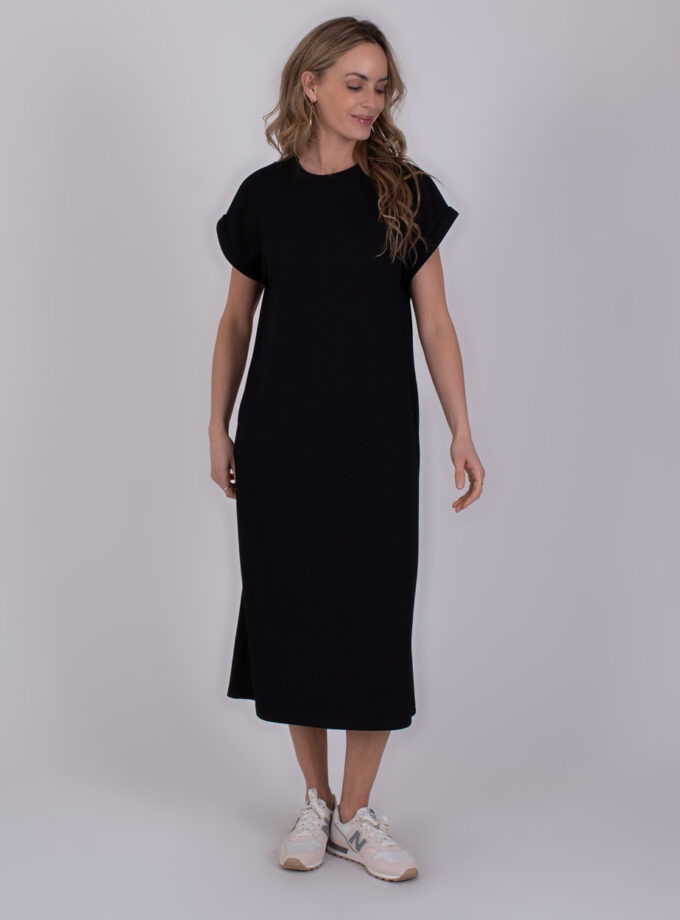 Vrouw draagt een zwarte Luanda-jurk met korte mouwen en witte sneakers.