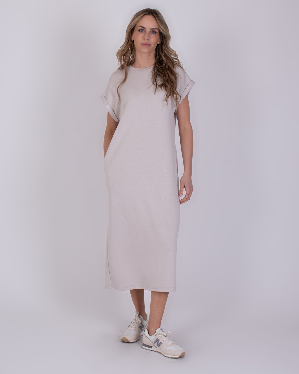 Vrouw draagt een beige, mouwloze midi-jurk uit de Luanda kit 1 met sportschoenen.