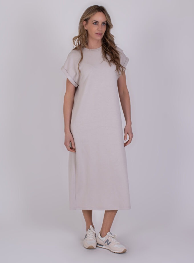 Vrouw draagt een lichtbeige, casual midi-jurk met opgerolde mouwen uit de Luanda kit 2, gecombineerd met witte sneakers.