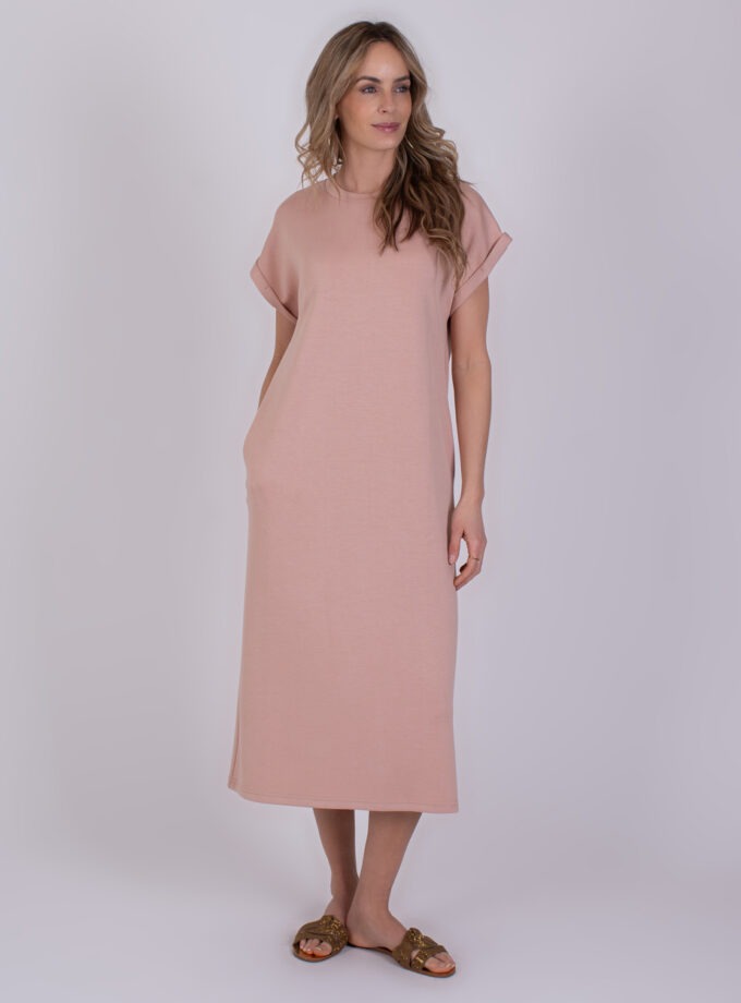 Vrouw draagt een losvallende, oudroze Luanda-jurk met korte mouwen en sandalen.