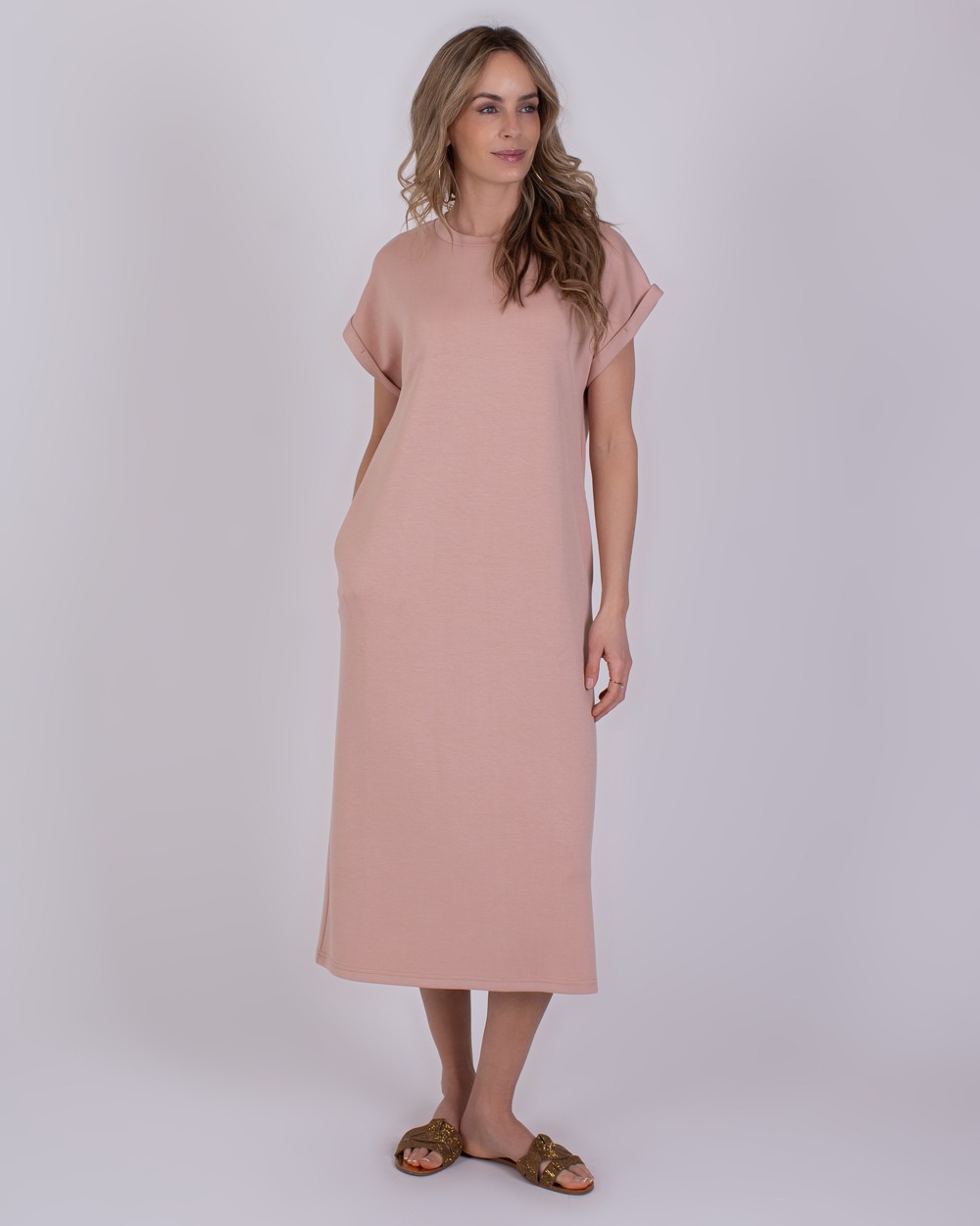 Vrouw draagt een losvallende, oudroze Luanda-jurk met korte mouwen en sandalen.