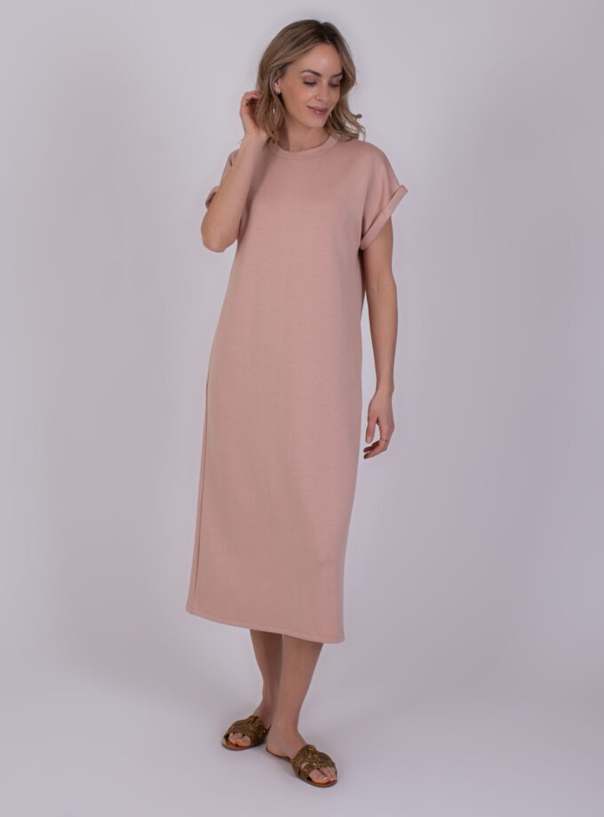 Vrouw draagt een losvallende, oudroze Luanda-jurk met opgerolde mouwen en sandalen.