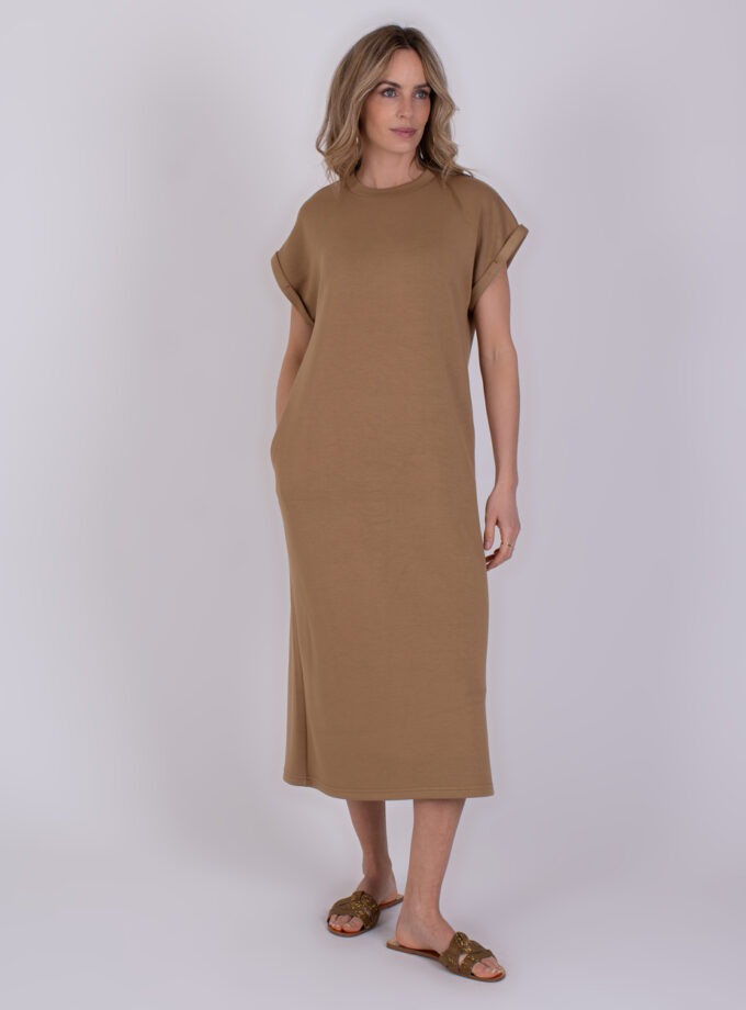 Vrouw draagt een taupekleurige Luanda-jurk met korte mouwen en sandalen.