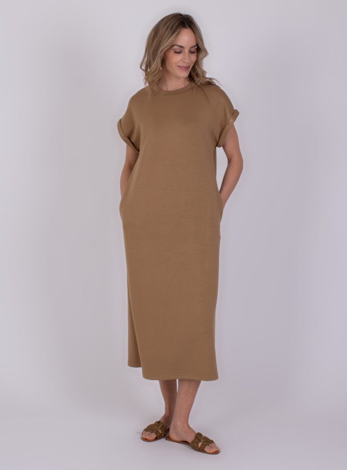 Vrouw draagt een taupekleurige Luanda-jurk met korte mouwen en sandalen.