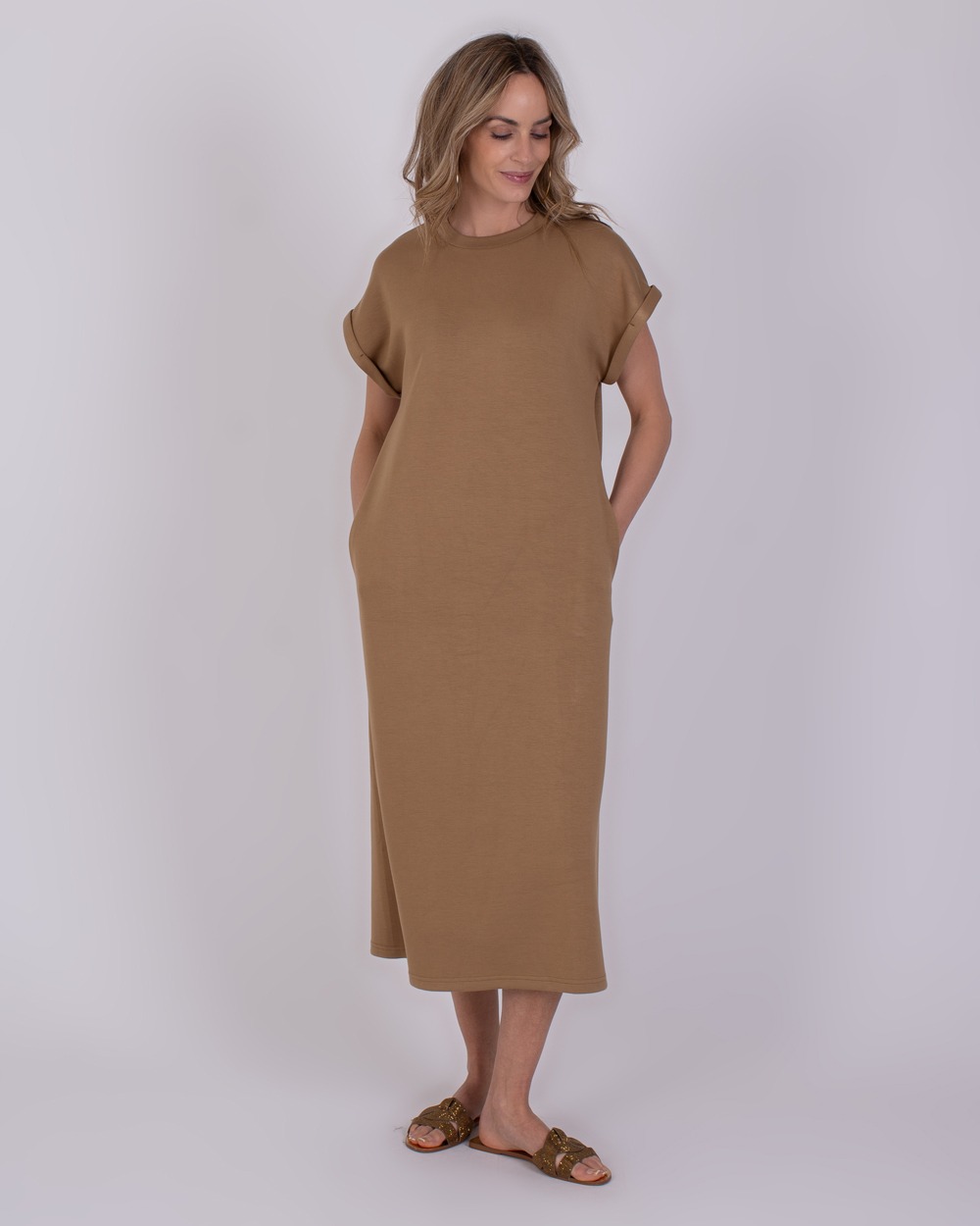 Vrouw draagt een taupekleurige Luanda-jurk met korte mouwen en sandalen.