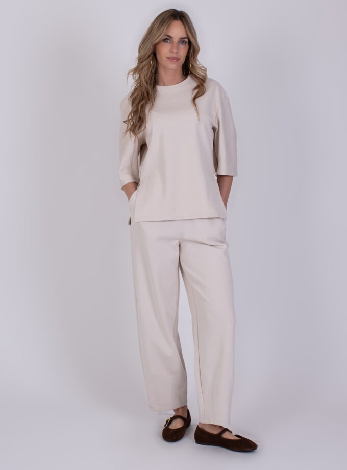 Vrouw draagt een comfortabele off-white loungewear set genaamd Malaga, met wijde broek en half mouw T-shirt.
