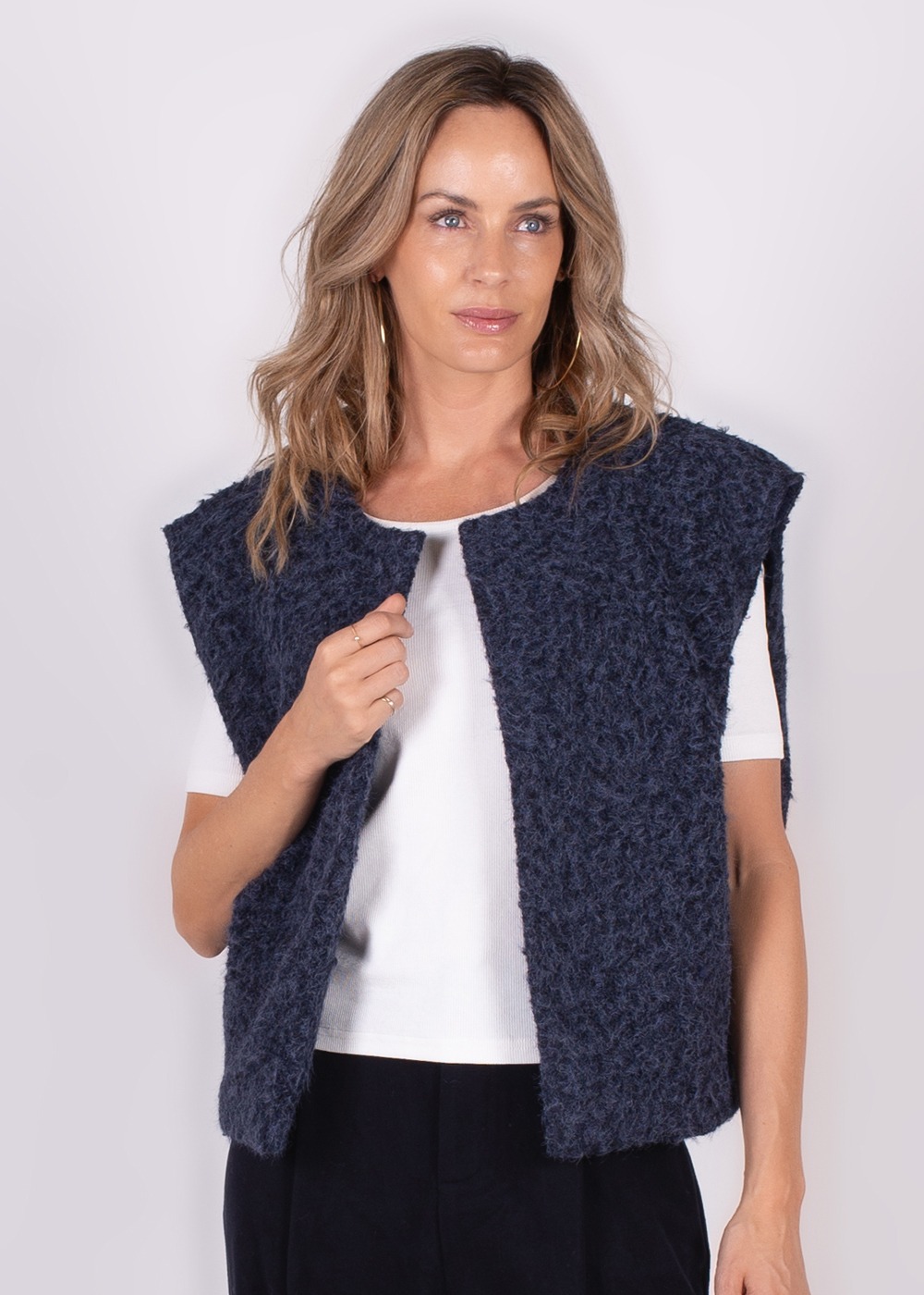 Een vrouw draagt een blauw, wollig Matsumoto gilet over een wit shirt, gefotografeerd vanuit een frontale hoek tegen een lichte achtergrond.